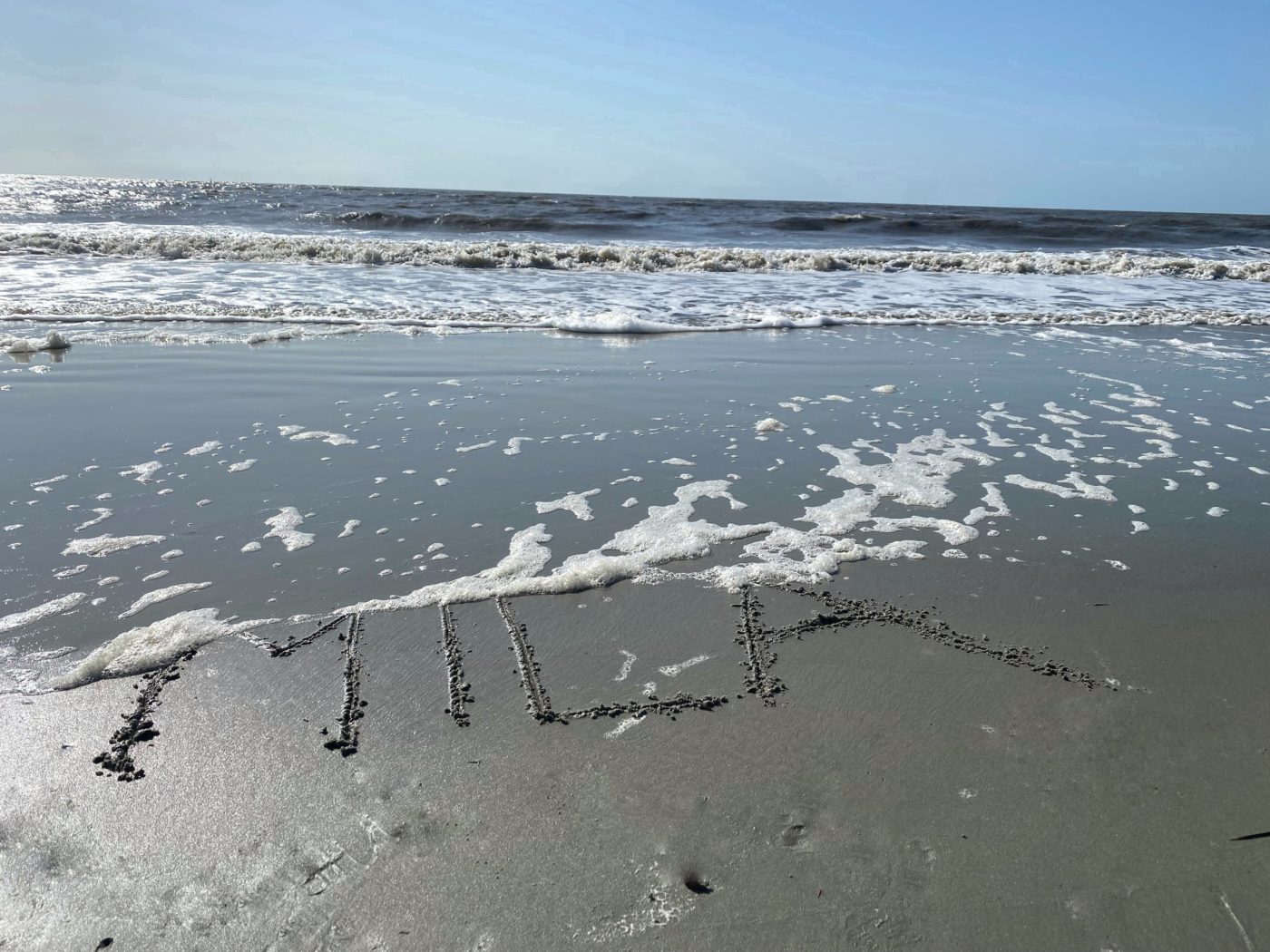 "Mila" written in wet sand at the beach